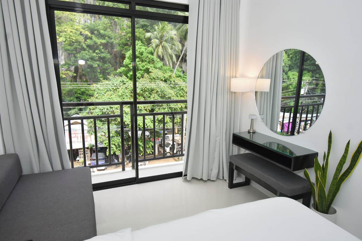 A hotel room with a large sliding glass door leading to a balcony, a bed, a bedside table, a mirror, and a potted plant.