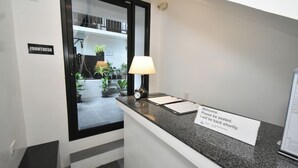 A reception desk with a sign indicating the front desk area, a clock, a lamp, and a window with a view of indoor plants. - BonBob Inn (El Nido)