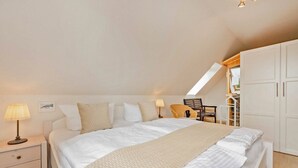 A bedroom with a large bed, a nightstand, a lamp, a chair, and a wardrobe.