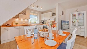 A modern kitchen with white cabinets, a wooden dining table set with plates, cups, and a bottle of water.