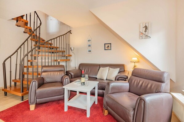 A modern living room with a staircase, leather sofas, a small white table, and a red carpet.