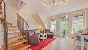 A spacious living area with a wooden staircase, a red rug, and a dining table with chairs.