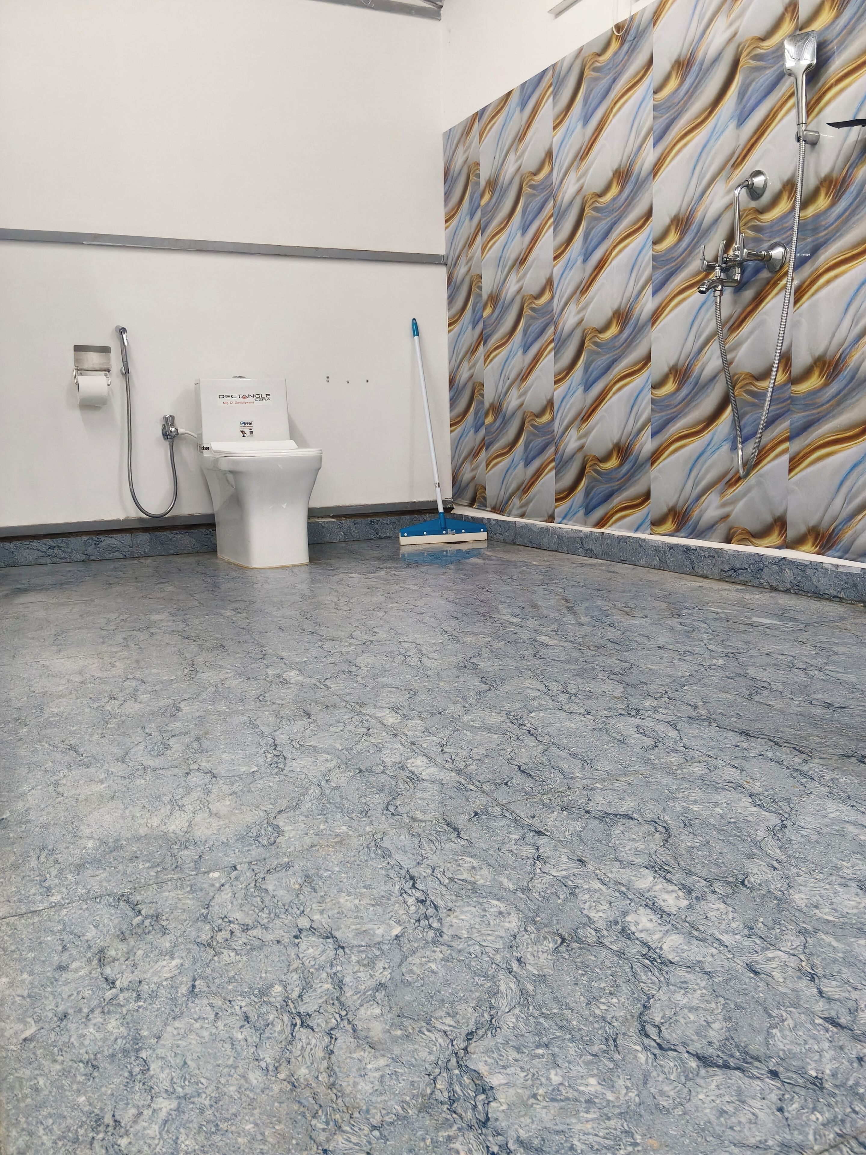 Un baño con piso de mármol, un inodoro, una ducha y una escoba apoyada en la pared.