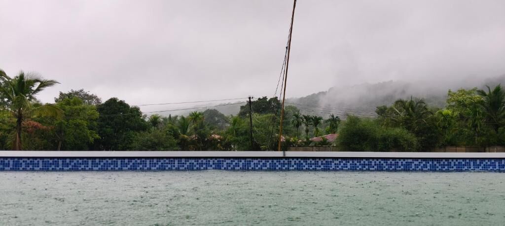 A view of a swimming pool with a tiled edge, surrounded by lush greenery and a misty mountain backdrop.