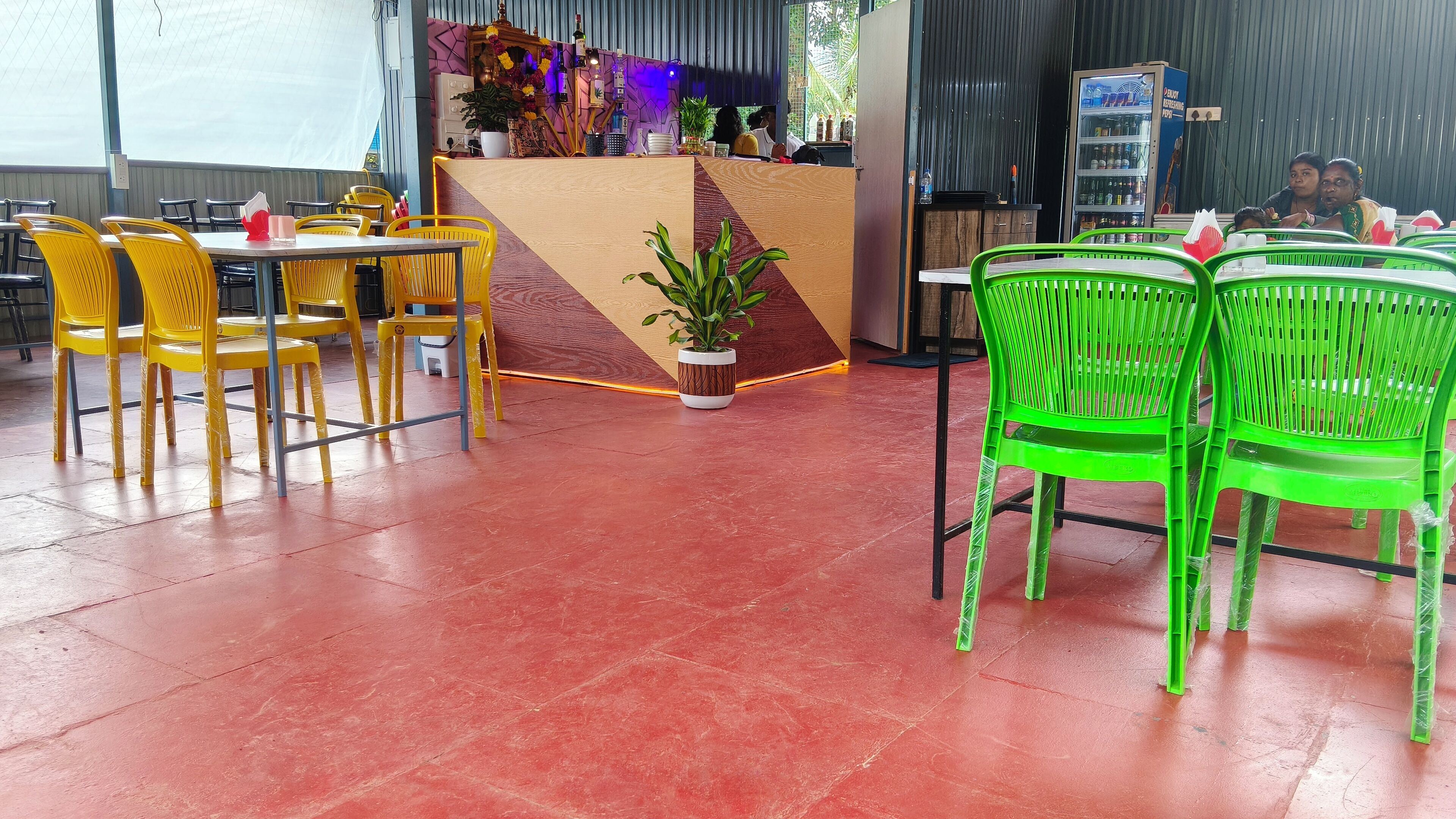 A restaurant with yellow and green chairs, a wooden counter, and a red floor.