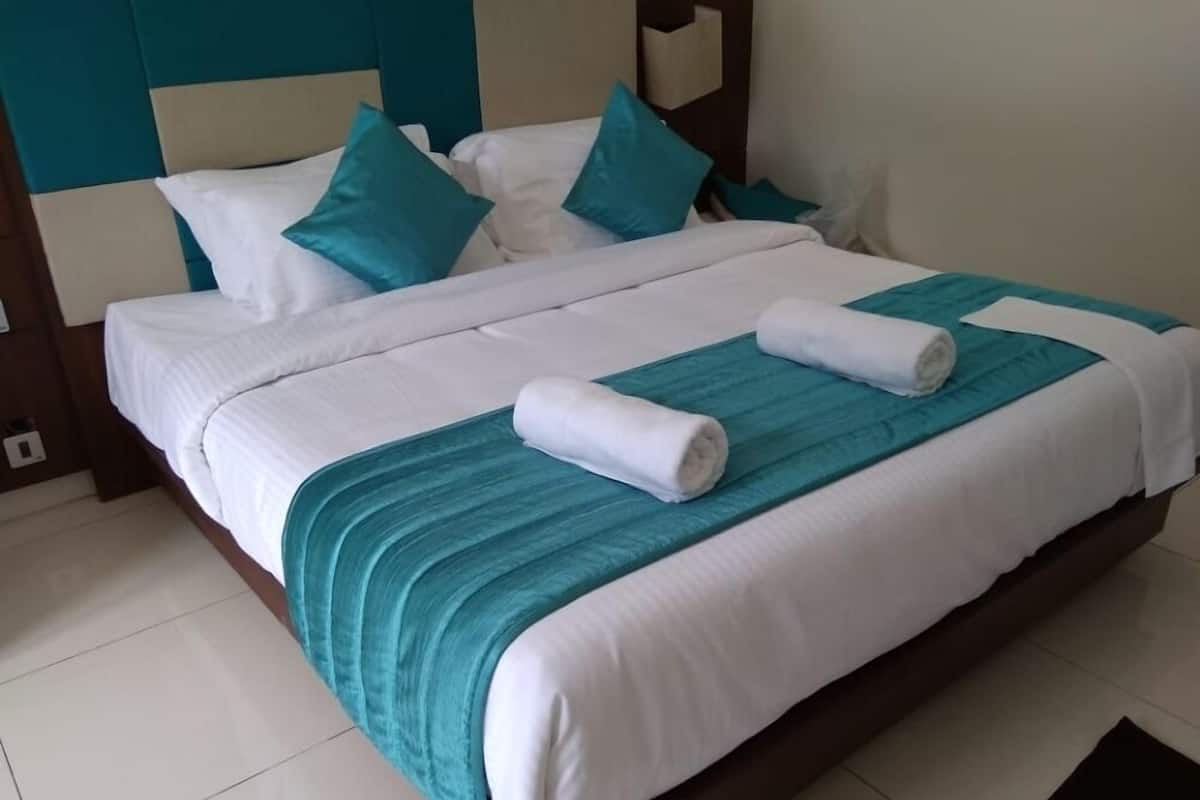 Una cama bien hecha con ropa blanca y azul turquesa, una manta azul turquesa y dos toallas enrolladas.
