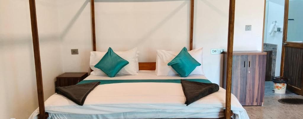 A four-poster bed with white and teal pillows, a wooden headboard, and a nightstand with a lamp.