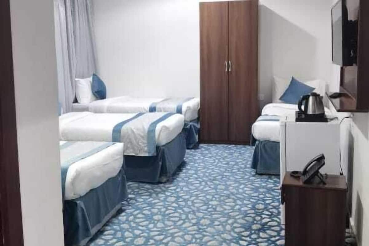 A hotel room with two beds, a wardrobe, a desk with a kettle, and a patterned carpet.