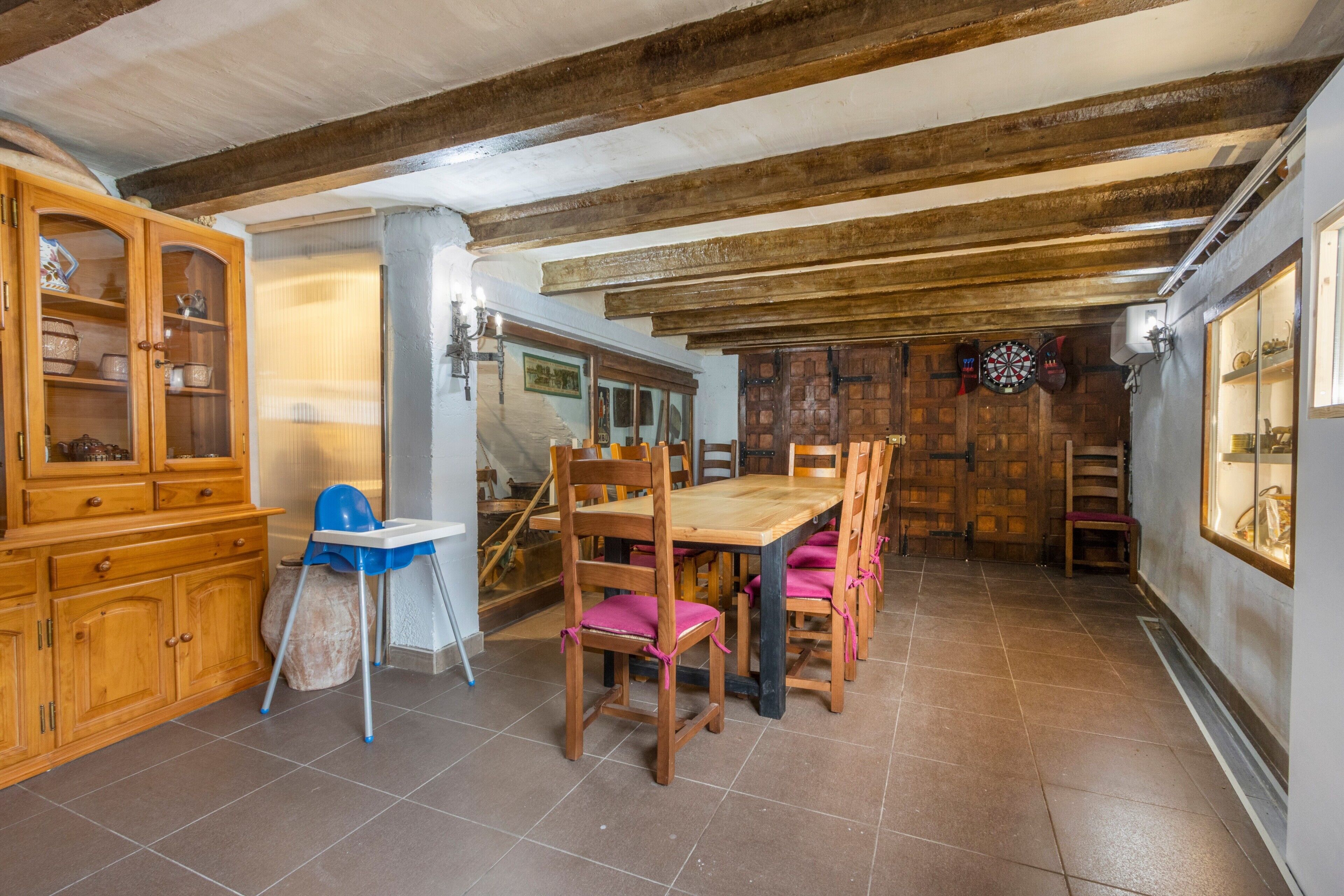 Un comedor con una mesa y sillas de madera, una trona azul y un mueble con puertas de cristal.