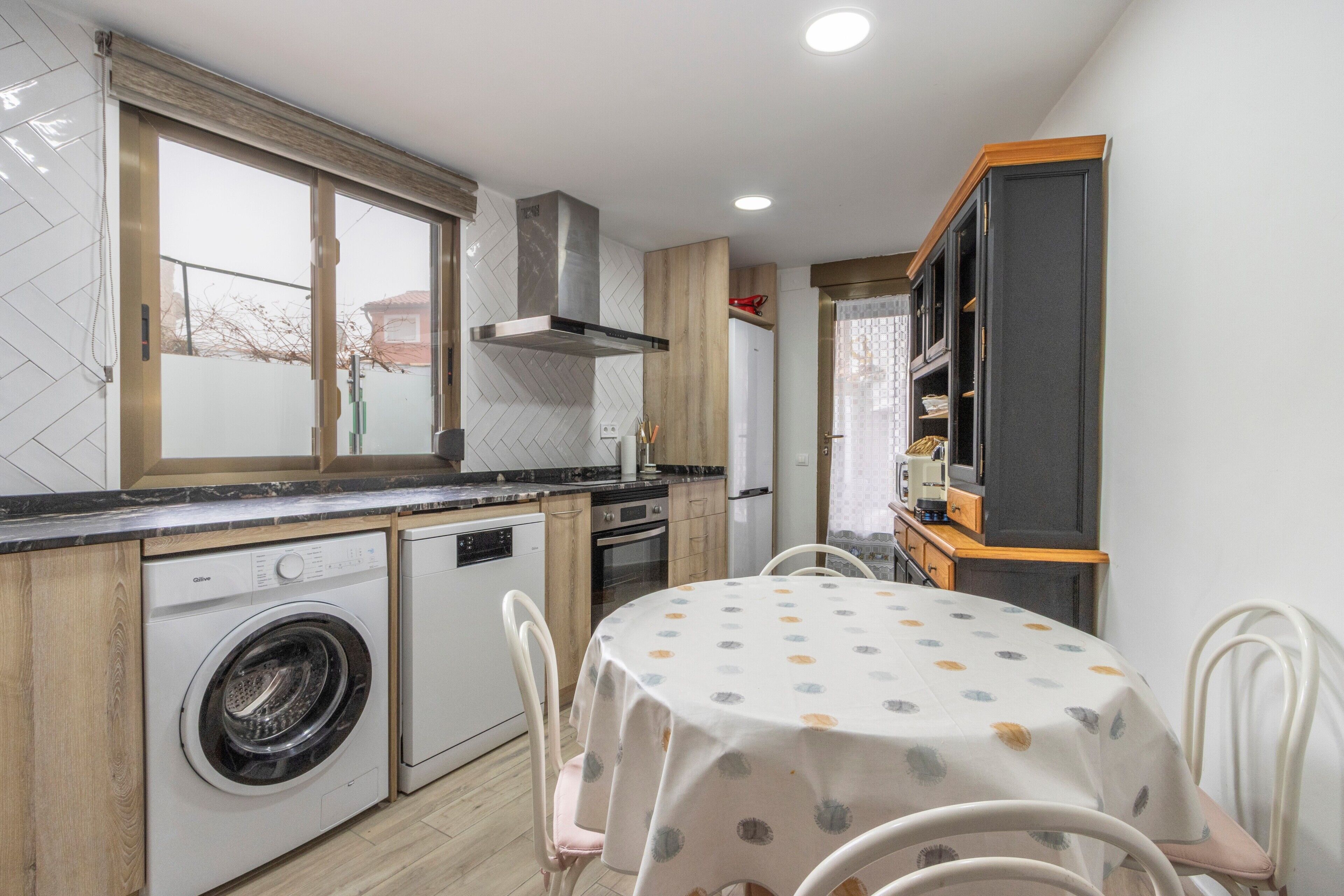 Cocina compacta con lavadora, mesa de comedor con sillas y horno integrado.