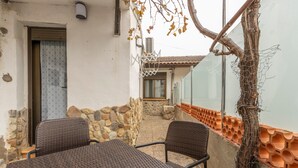 Une terrasse avec des meubles en osier, un mur en pierre et une vue sur une maison.