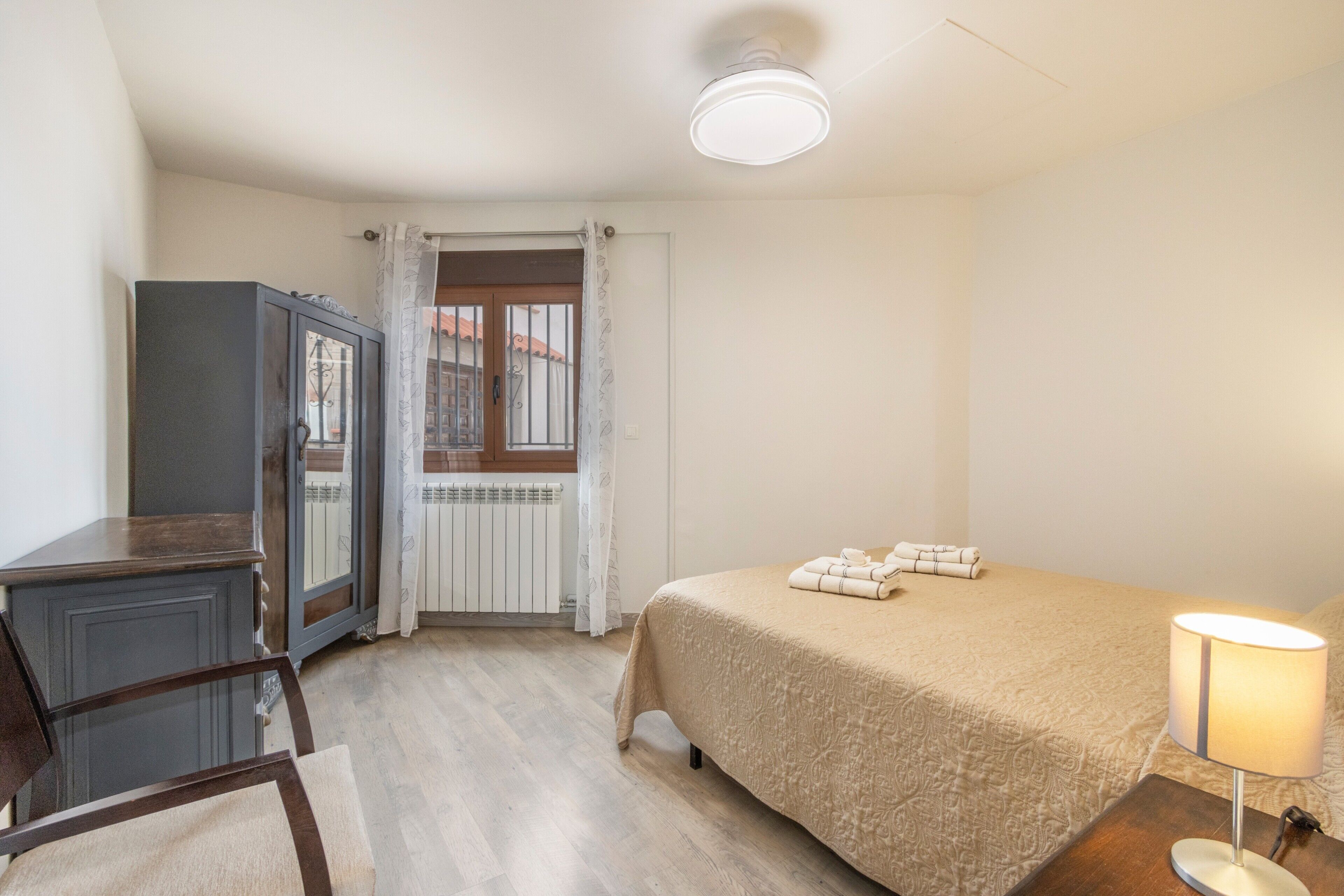 Une chambre à coucher avec un lit, un bureau, une chaise, une lampe et une fenêtre avec des rideaux.