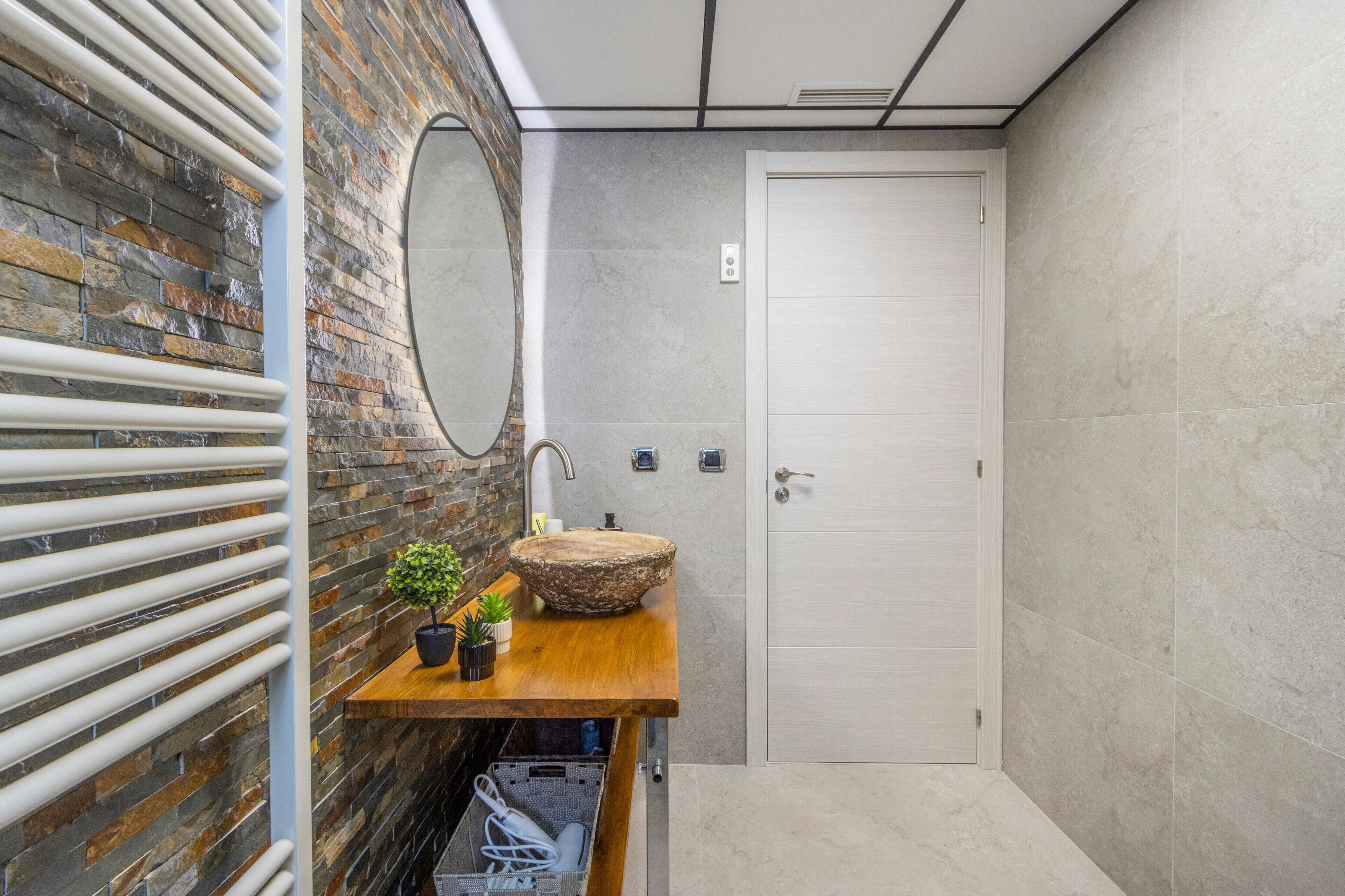 Une salle de bain avec un meuble-lavabo en bois, un lavabo rond, un miroir et une porte.