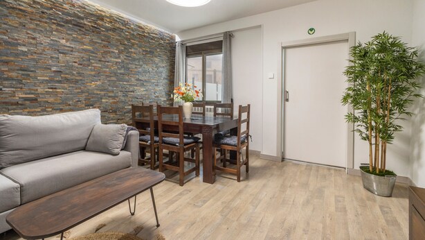 Un salon moderne comprenant un canapé, une table à manger, des chaises, un banc, une plante en pot et un mur en briques.