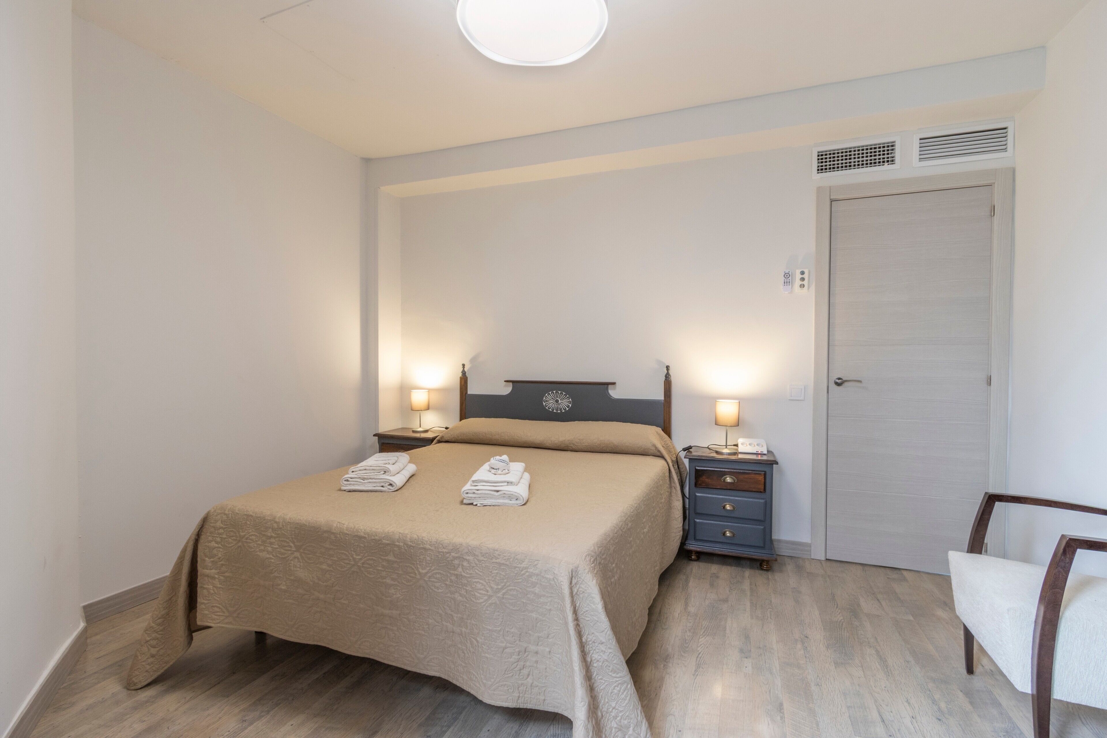 A bedroom with a bed, bedside lamps, a chair, a wardrobe, and a door.