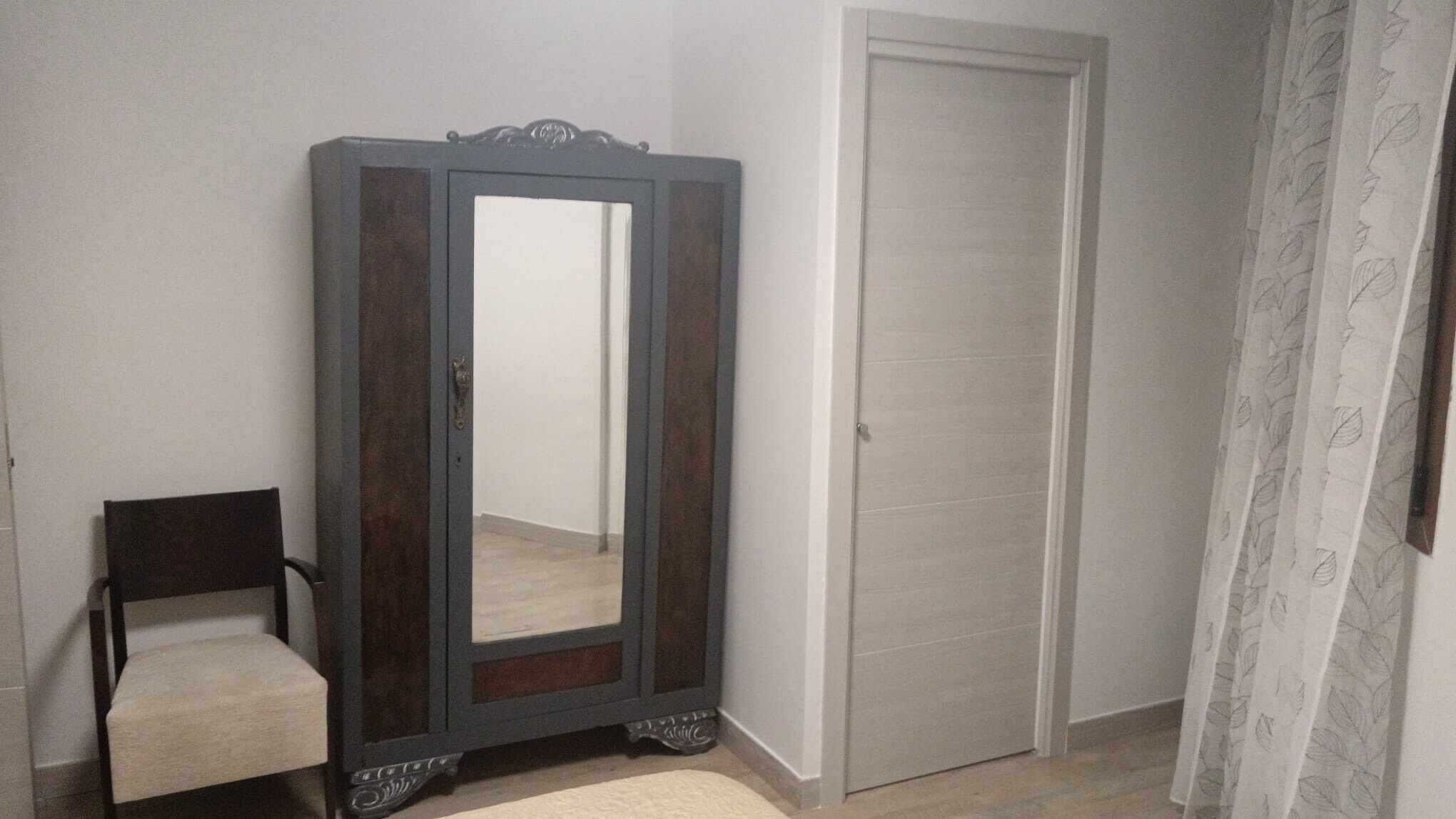 Una habitación con un espejo grande, una silla, una puerta y una cortina.