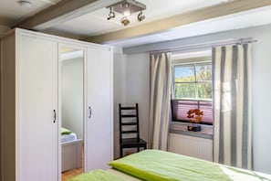 Un dormitorio con cama, una silla, una ventana con cortinas y un armario.