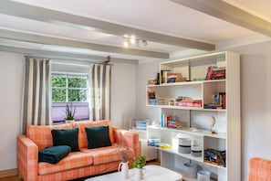 Una sala de estar con un sofá, una mesa de centro, una estantería y una ventana con cortinas.
