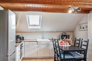 Eine Küche mit Fenster, einem Esstisch mit Stühlen, einem Kühlschrank und einem Spülbecken.