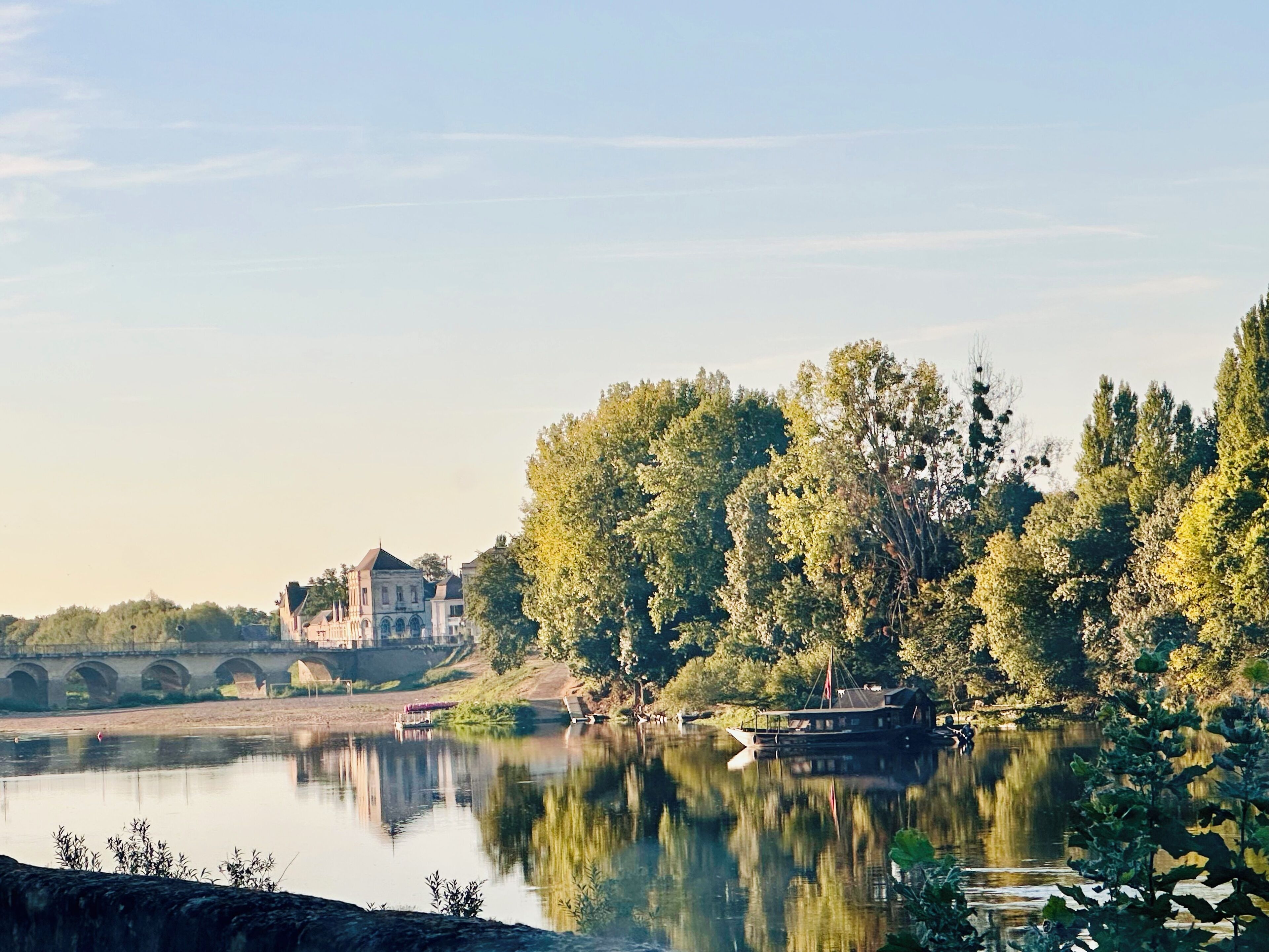 A serene riverside scene with a bridge, a boat, and a building with a distinct architectural style.