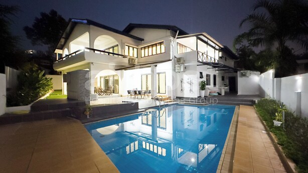 Una casa de dos pisos con piscina, balcón y un espacio exterior bien iluminado.