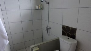 A bathroom with a shower, toilet, and a small shelf with toiletries. - The Studio at Warung Bambu Pemaron (Buleleng)