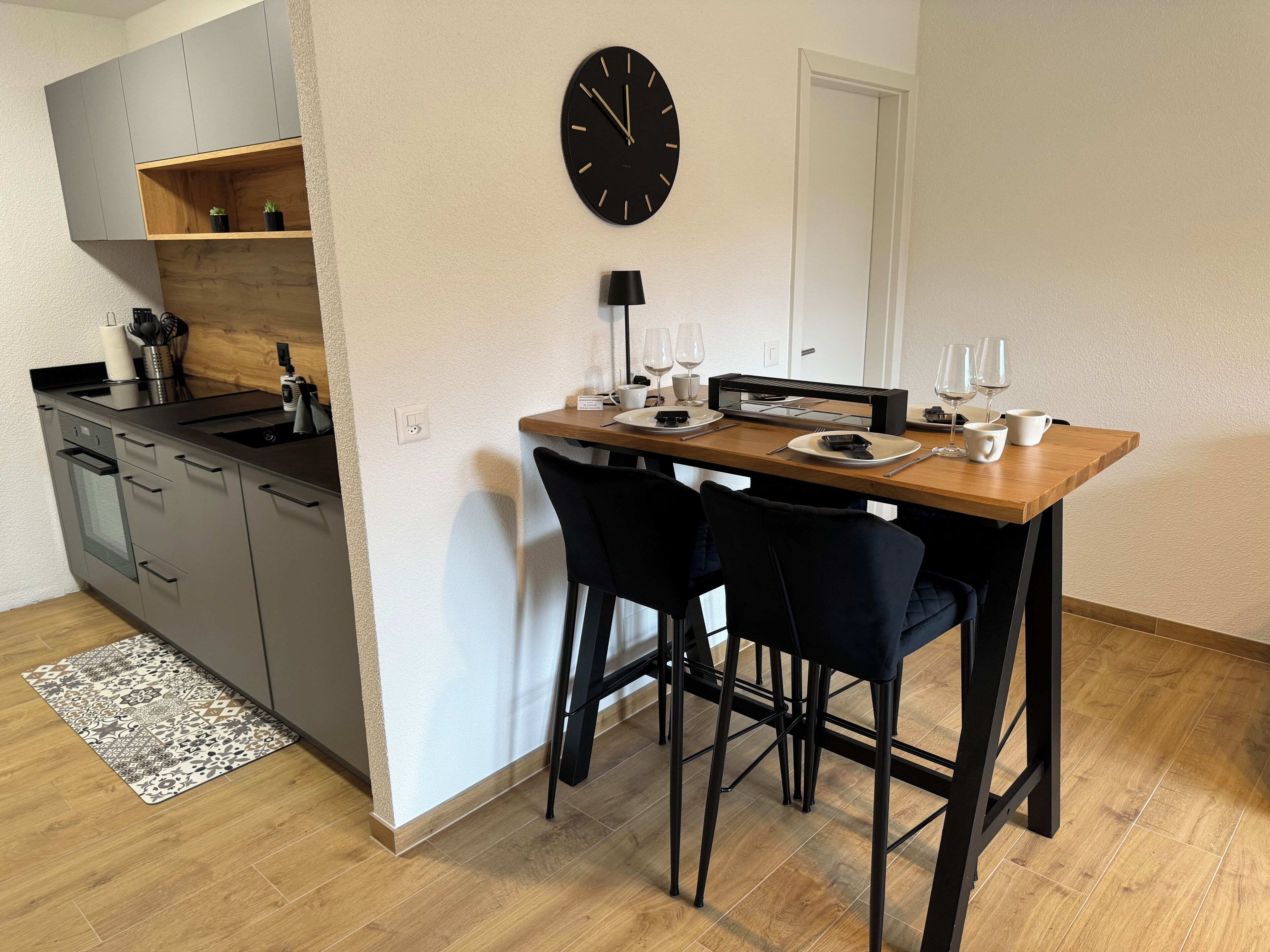 Una cucina moderna con mobili grigi, un piano di lavoro in legno e un orologio nero appeso al muro.