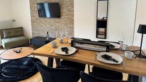 Una sala de estar moderna con una pared de piedra, un televisor de pantalla plana, una mesa de comedor con platos, vasos y cubiertos, y un sofá.