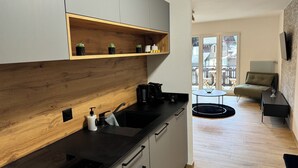 Una cocina moderna con detalles de madera, una cafetera y vistas al área de estar con una mesa redonda y un sofá.