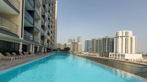 A swimming pool with lounge chairs and umbrellas, surrounded by high-rise buildings. - Mesmerizing Canal View Studio with private Jacuzzi (Dubai)
