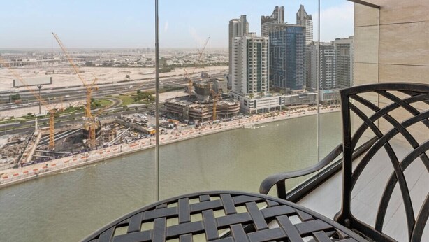 A balcony with a view of a river, construction cranes, and high-rise buildings. - Mesmerizing Canal View Studio with private Jacuzzi (Dubai)