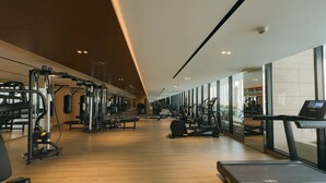 A modern gym with cardio machines, weight stations, and a large window providing a view of the city. - Mesmerizing Canal View Studio with private Jacuzzi (Dubai)