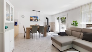 A modern living room with a sectional sofa, a dining area with chairs and a table, and a kitchen area with cabinets and a stove.