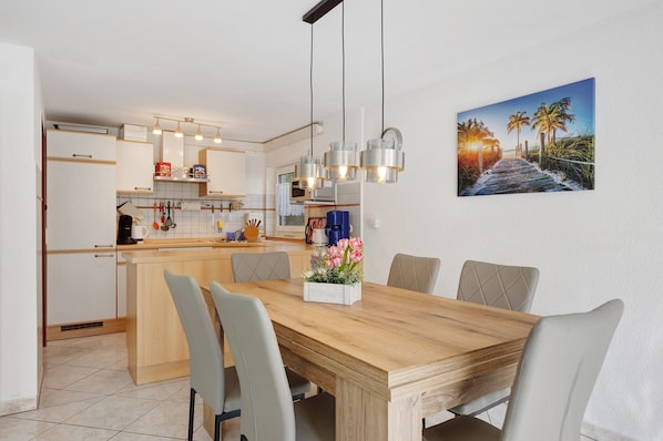 A modern kitchen with white cabinets, a wooden dining table, and pendant lights.