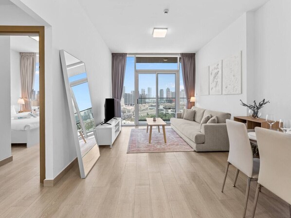 A modern living room with a sofa, a coffee table, a TV, and a dining area with chairs.