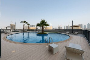 A rooftop pool with palm trees, lounge chairs, and a city skyline in the background.