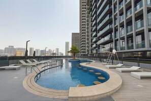 A rooftop swimming pool with lounge chairs, a palm tree, and a city skyline in the background.
