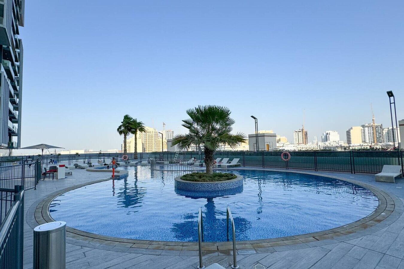 A rooftop pool with a palm tree, lounge chairs, and a cityscape in the background.