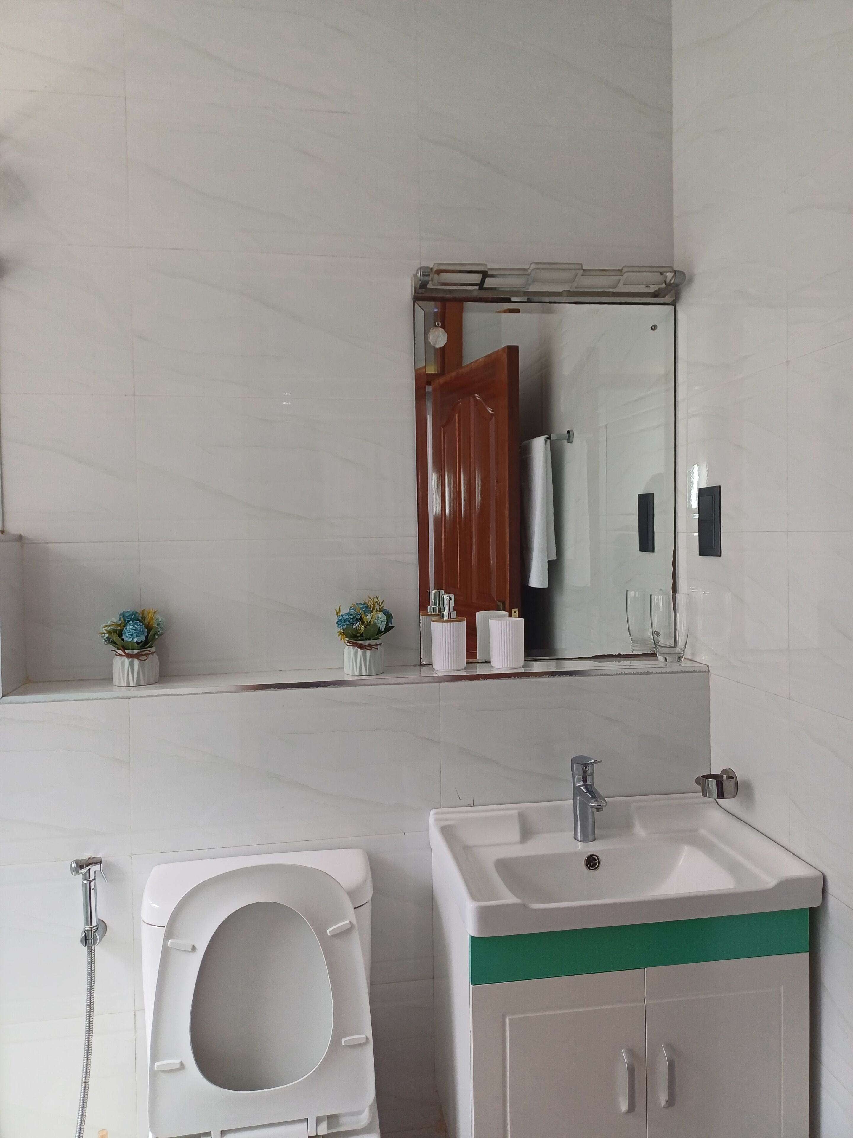 A bathroom with a toilet, sink, mirror, and two small flower vases on the countertop.