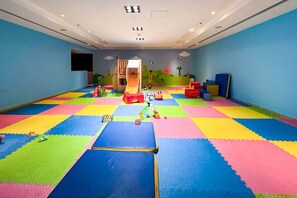 Una sala de juegos con coloridos tapetes de espuma, un tobogán y distintos juguetes.