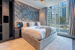 A modern bedroom with a large bed, a built-in wardrobe, a flat-screen TV, and a city view.