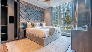 Une chambre moderne dotée d’un grand lit, d’étagères intégrées, d’un téléviseur à écran plat et offrant une vue sur la ville grâce à de grandes fenêtres.