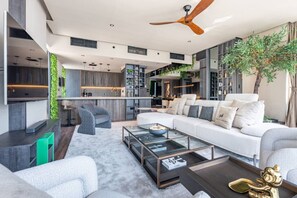 A modern living room with a glass coffee table, a sofa with patterned cushions, and a ceiling fan.