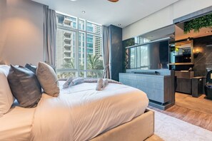 A modern bedroom with a large bed, a built-in desk, and a view of a cityscape.