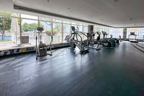 Een fitnessruimte met cardiotoestellen, grote ramen en uitzicht op buiten.