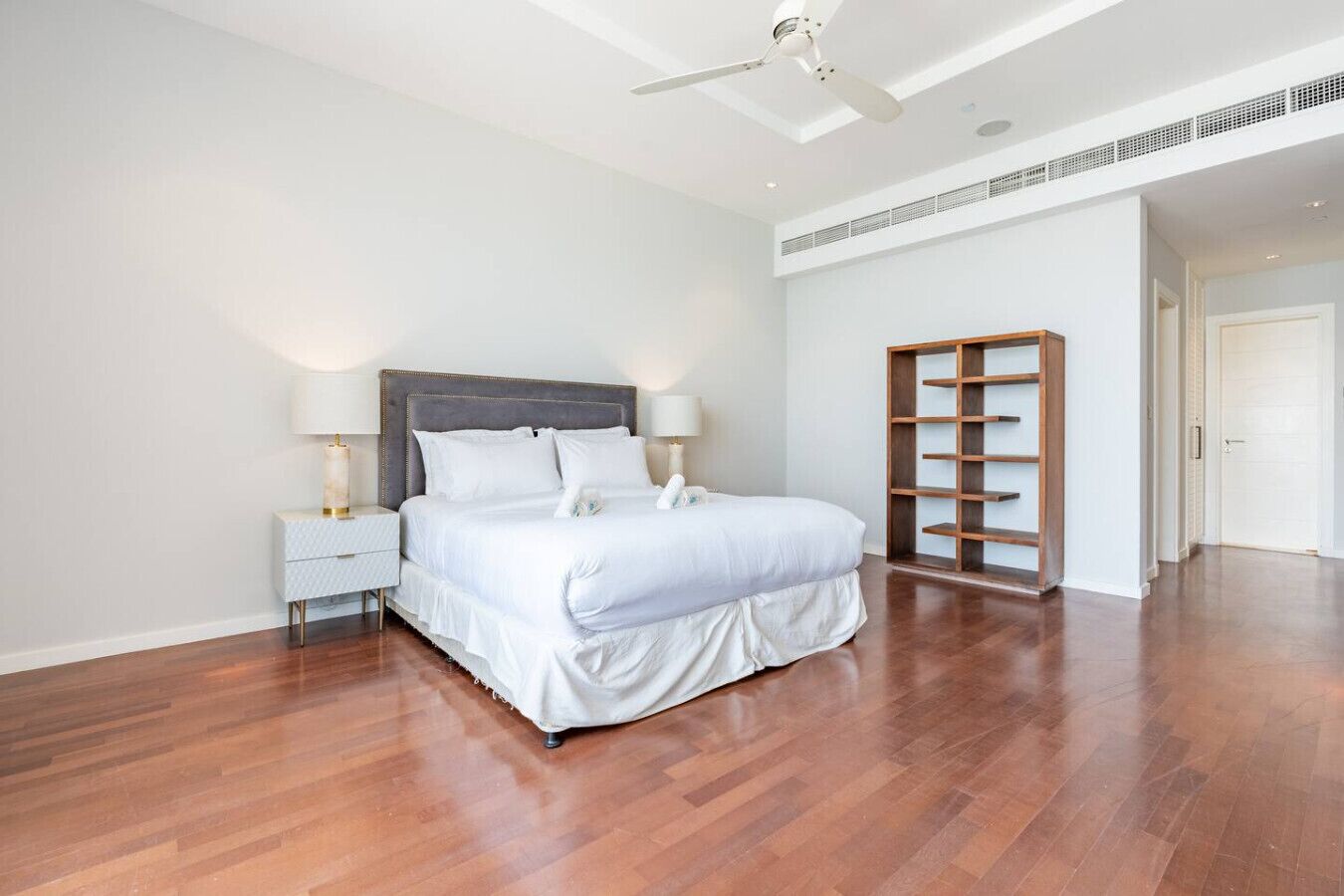 Une chambre moderne avec un grand lit, une table de chevet, un ventilateur de plafond et une étagère en bois intégrée.