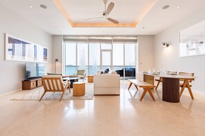 A modern living room with a large window, a ceiling fan, and a dining area with a table and chairs.