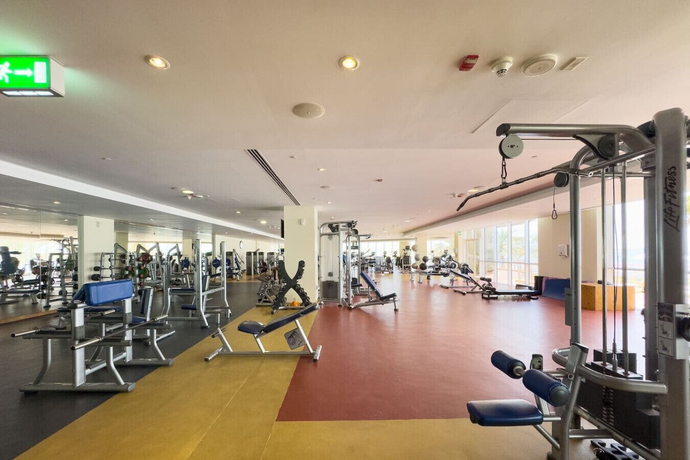 Ein Fitnessstudio mit verschiedenen Trainingsgeräten, Spiegeln und einem roten Teppichboden.