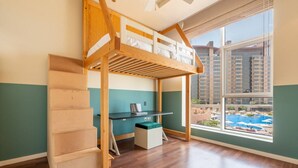 Quarto com cama beliche, escrivaninha e janela com vista para uma piscina e edifícios.