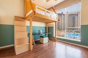 Una habitación con cama tipo litera, un escritorio y ventana con vistas a una piscina y edificios.